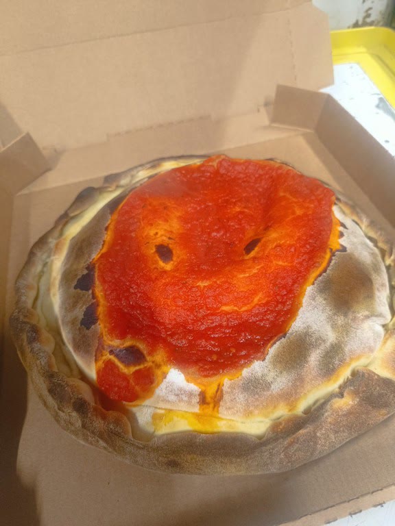 Une pizza soufflée nappée de sauce tomate dans sa boîte